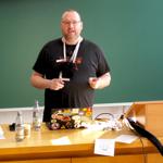 Picture of a lecture room. Chris standing in front of a blackboard in a dynamic pose.